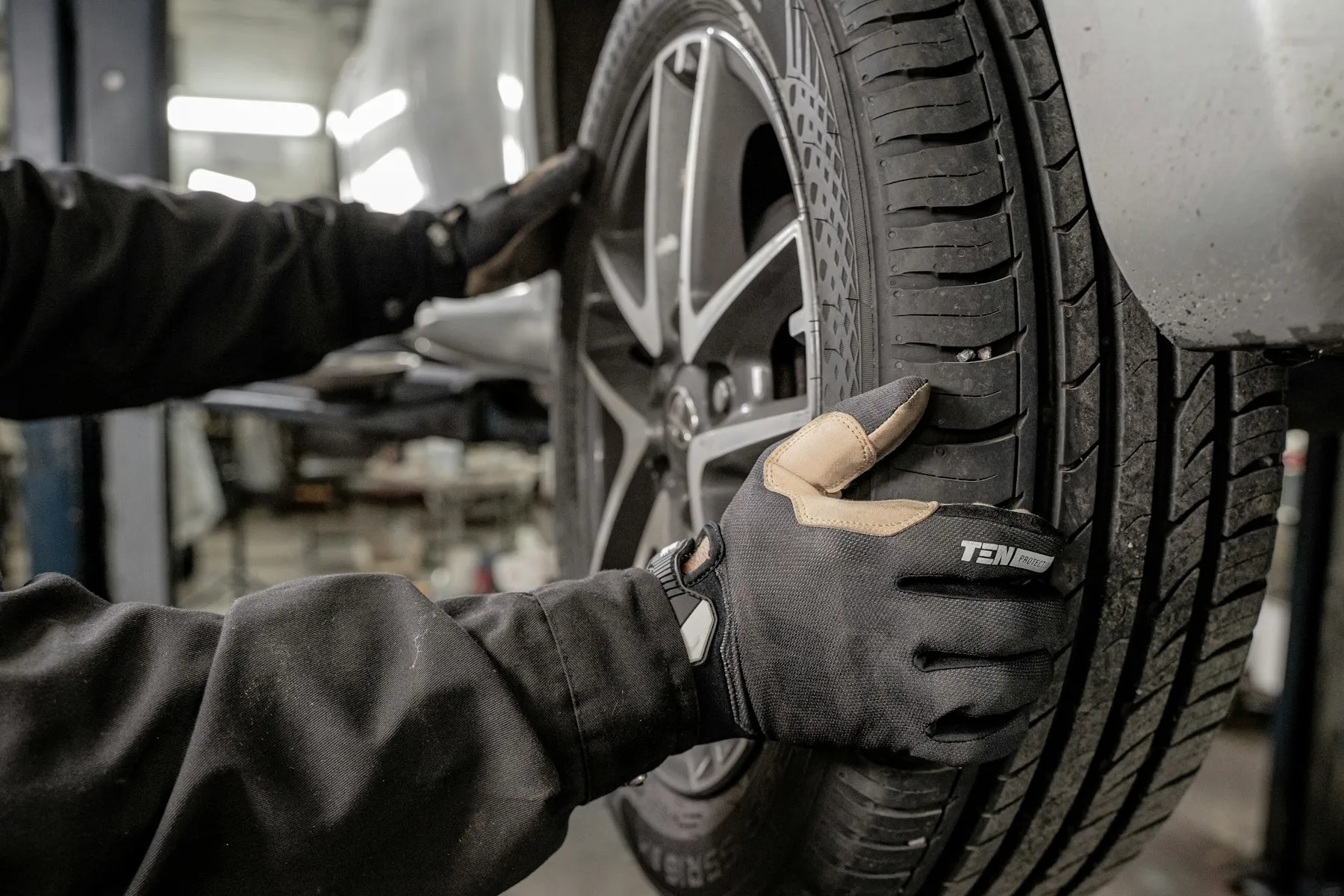 Hände mit Arbeitshandschuhen am Rad eines Fahrzeugs auf der Hebebühne, das Reifenprofil im Fokus